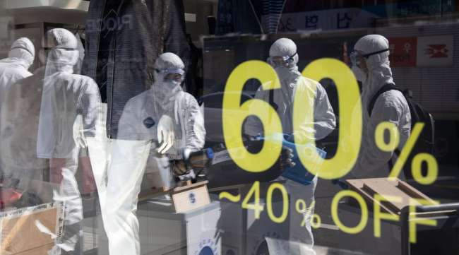 Workers wearing protective suits are reflected in a glass window of a clothing store in Seoul, South Korea, on Feb. 27.
