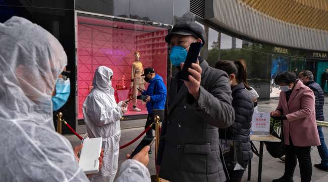 Workers wearing protective suits check customers' health QR codes at the entrance of a re-opened shopping mall in Wuhan, China.