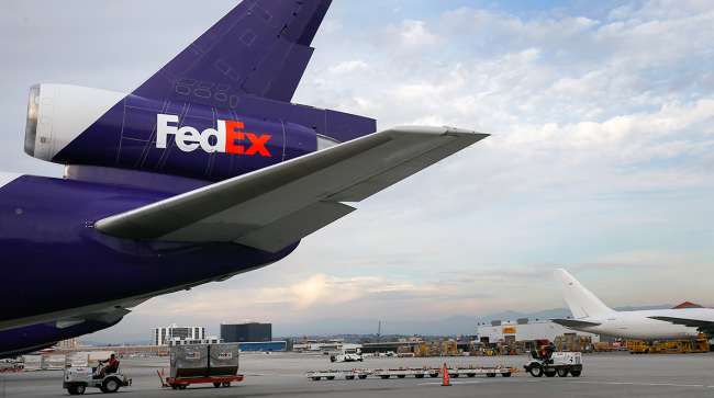 Employees drive carts on the tarmac past a cargo plane waiting to be loaded with shipments at the FedEx Corp. distribution hub at Los Angeles International Airport (LAX) in Los Angeles.