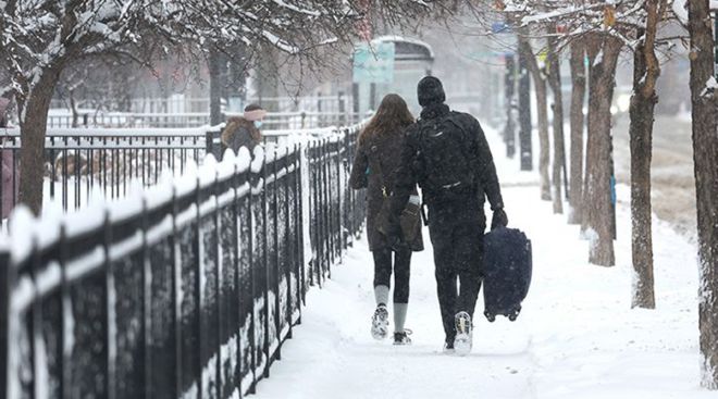 People carry luggage down a snow-covered sidewalk