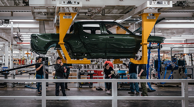 A Rivian pickup truck is suspended as employees work on the vehicle