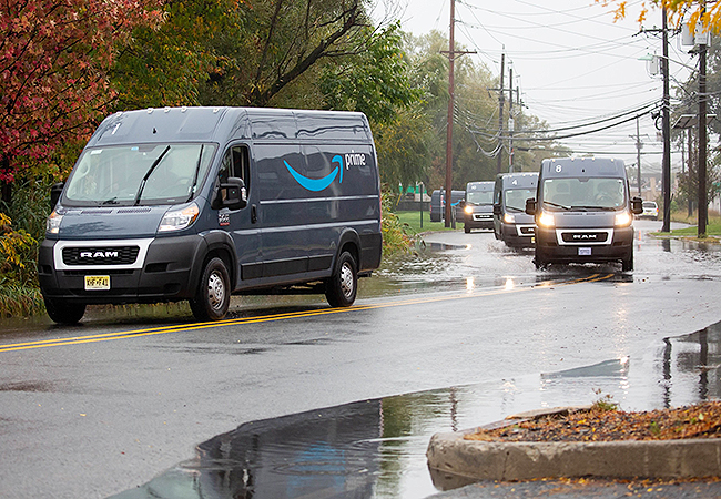 On a rainy day, Amazon vans navigate a street in a New Jersey neighborhood.