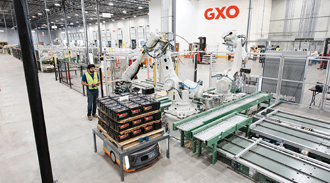 A GXO employee watches as a robot sorts items