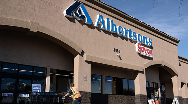 A worker pushes shopping carts outside an Albertsons supermarket in Las Vegas, Nev.