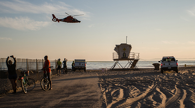 A helicopter flies over bystanders gathered at the beach during an oil spill in Huntington Beach on Oct. 3.