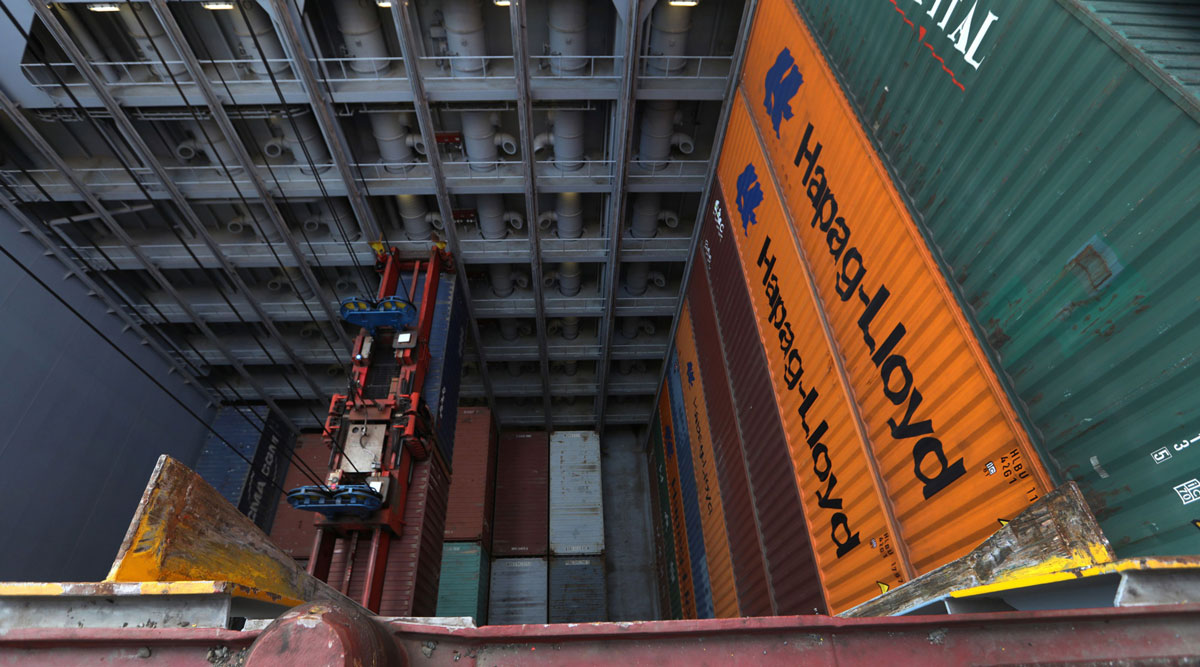 A pair of shipping containers hang from a ship-to-shore crane while a Hapag-Lloyd ship is unloaded.