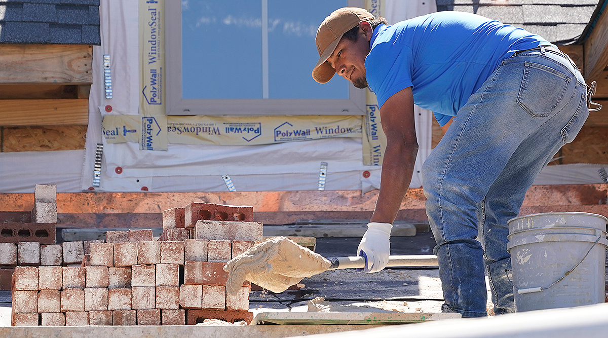 A mason shovels a cement mixture as he prepares to lay down bricks on the exterior wall of a new house in Flowood, Miss.