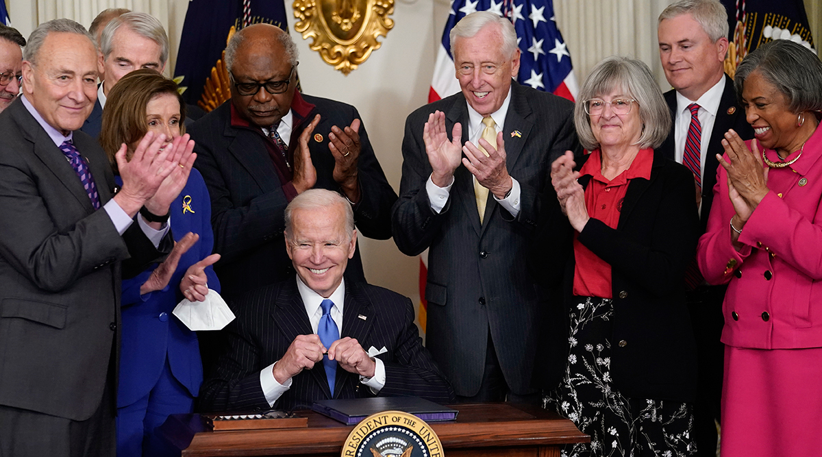 President Biden surrounded by members of Congress, signs Postal Bill