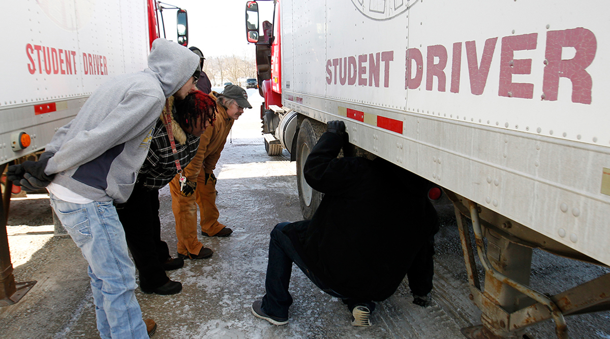 Student drivers look under a truck's trailer