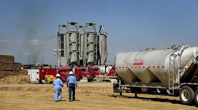 Workers walk toward Halliburton "sand castles" at an Anadarko Petroleum Corp. fracking site near Dacono, Colo., in August 2014.