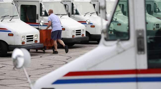 A USPS employee loads a mail delivery vehicle