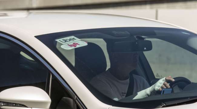 Lyft and Uber logos are displayed on the windshield of a vehicle at LAX.