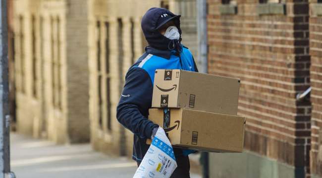 A worker wearing a protective mask and gloves carries Amazon boxes during a delivery in New York on March 26.