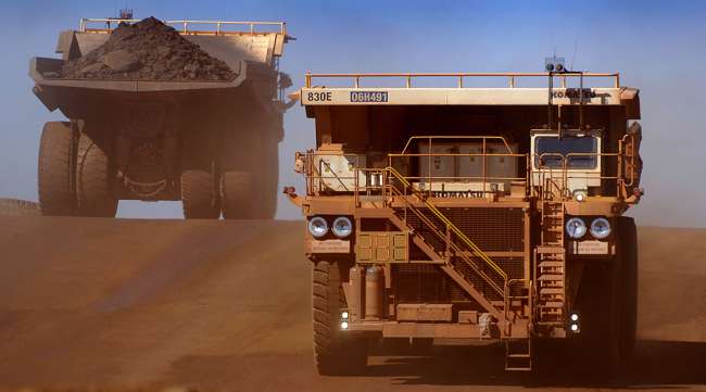 Heavy earth moving trucks at the Tom Price iron ore mine, operated by Rio Tinto Group, are lit up by the afternoon sun in Pilbara, north Western Australia.