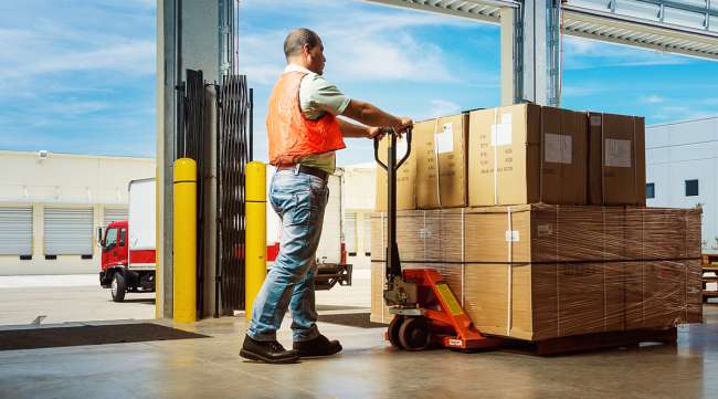 A worker pushes a hydraulic hand pallet truck at a warehouse