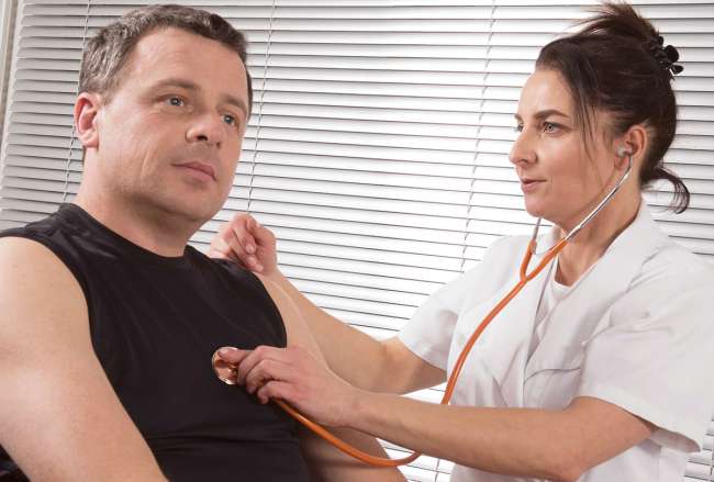 A health professional checks a driver’s heart and lungs during a medical exam.