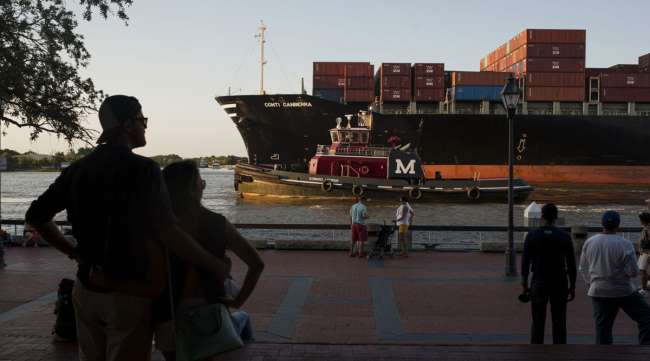 Pedestrians watch as a cargo ship and tug boat make their way into the Port of Savannah in 2015.
