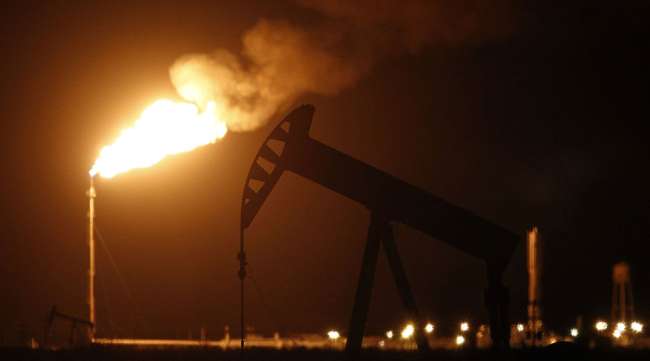 The silhouette of an electric oil pump jack is seen near a flare in the oil fields surrounding Midland, Texas.