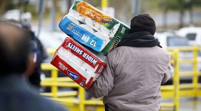 A shopper carries paper towels and toilet paper from a Costco