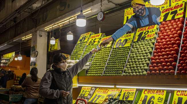 A vegetable vendor hands change back to a customer at the Central de Abastos Market in Mexico City, Mexico