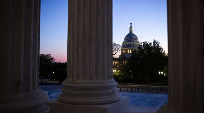 The U.S. Capitol stands past columns of the Supreme Court in Washington on April 16.