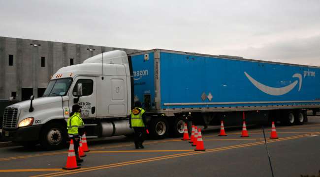 An Amazon Prime truck passes workers controlling traffic outside an Amazon fulfillment center.