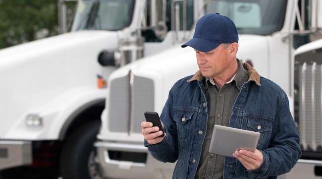 Truck driver using cellphone and tablet in front of trucks