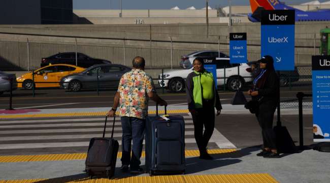 A passenger pulls bags while waiting for a ride at the Uber pickup area at LAX in October 2019.