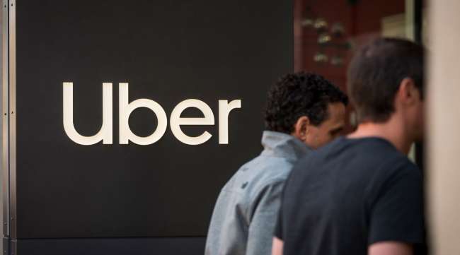 Pedestrians pass in front of signage displayed outside Uber headquarters in San Francisco.