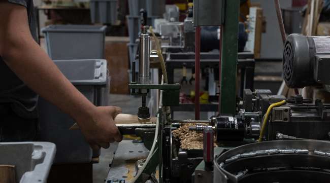 A worker shapes and drills a wooden tap handle