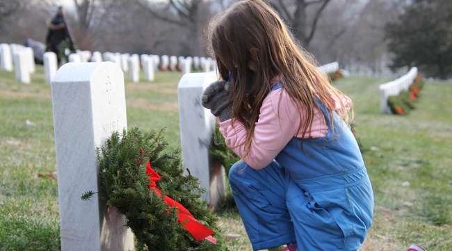 Girl kneels next to stone during Wreaths Across America Day 2020