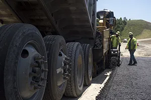 A truck dumps asphalt as contractors pave a road