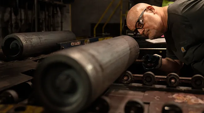 A steel worker inspects a 155 mm M795 artillery projectile