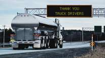 Truck passing under sign thanking truck drivers on road
