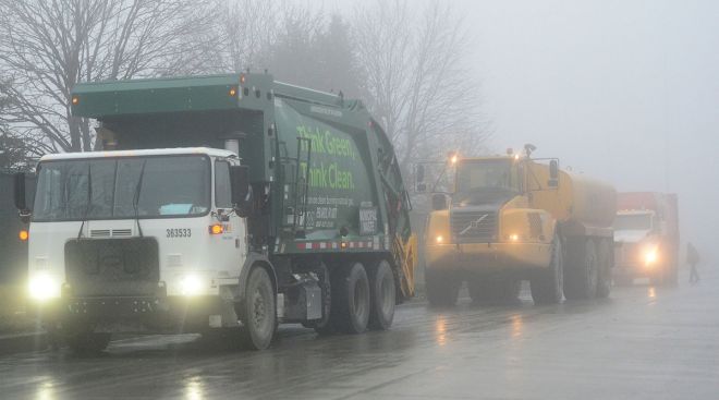 A recycling vehicle leads a caravan of trucks down a foggy road