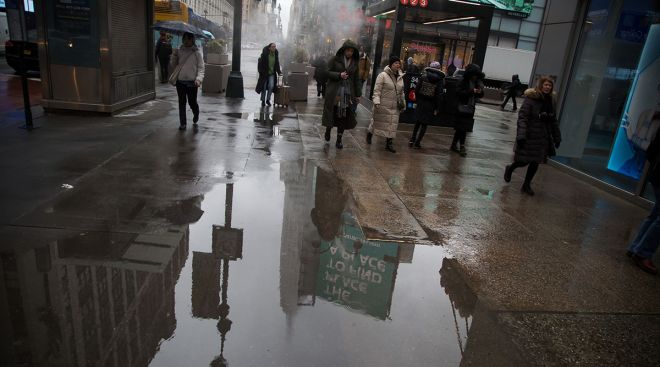 Pedestrians pass a puddle of melted snow
