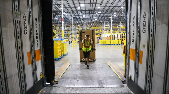 An Amazon employee loads a pallet of snack foods into a semi truck trailer.