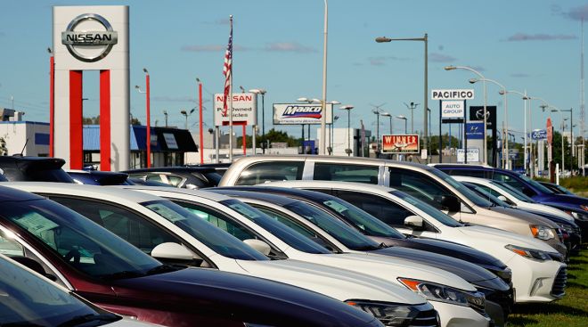 Cars for sale line the road at a used auto dealership