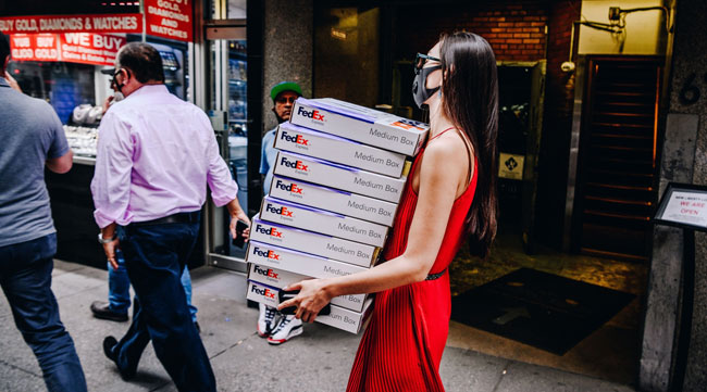 A pedestrian wearing a mask carries FedEx boxes in New York on June 10.